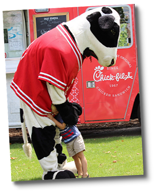 Chick-fil-A Cow hugging child in front of Chick-fil-A Food Truck